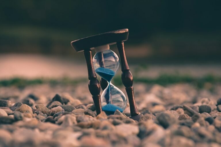 Hourglass with blue sand resting on small pebbles