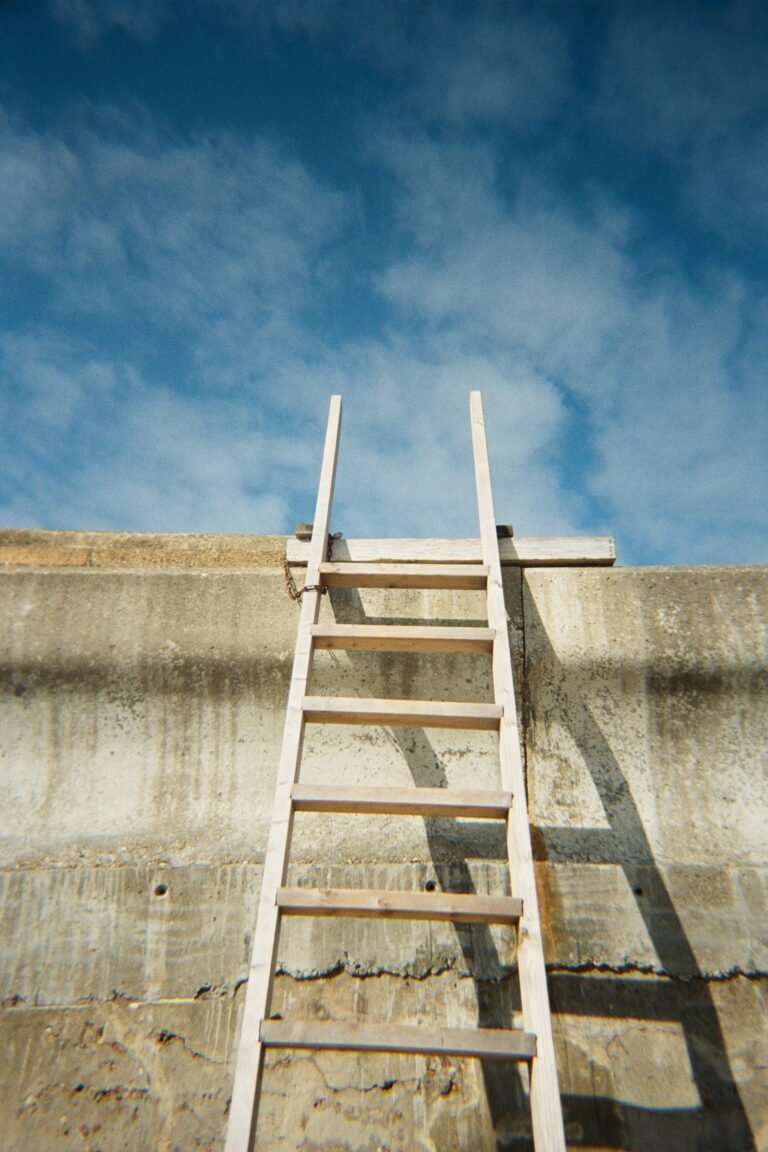 Aluminum ladder extending above the top edge of a concrete wall against a blue sky