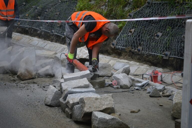 A construction worker in an orange safety vest cutting stone blocks on a job site